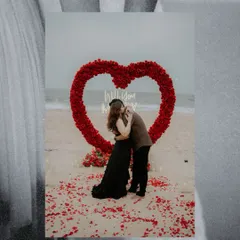 A deeply romantic beach proposal. The couple embraces within a large heart made of red roses, with the ocean in the background, creating an unforgettable and picturesque moment.