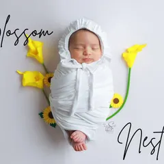 A baby peacefully sleeping, wrapped in a pure white swaddle and bonnet. The simple yellow flowers add a delicate touch of color to this serene and classic "potato sack" pose.
