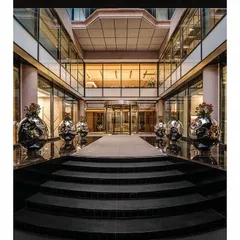 A symmetrical view of the grand entrance to 'The Layered Office'. The design creates a formal approach with a central walkway flanked by large, sculptural stainless steel pots, leading into the central courtyard.