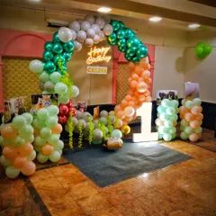 This jungle-themed decoration for a first birthday uses a soft, earthy color palette of green, orange, and white balloons. The arrangement includes a large light-up number '1' and is designed to create a fun, safari-like atmosphere for the little one's big day.