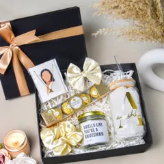 A high-angle shot of a bridesmaid proposal box. The elegant black and gold theme, combined with items like a custom candle and chocolates, creates a luxurious and inviting image.