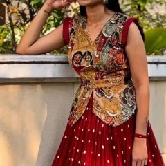 This unique dandiya outfit features a Kalamkari print blouse paired with a deep red georgette skirt with small embellishments. It's a stylish fusion of traditional art and modern design, perfect for making a statement.