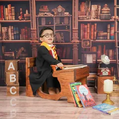 Ready to cast a spell. The vintage school desk and bookshelf backdrop create an authentic Hogwarts classroom feel for this themed baby photoshoot.