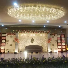 A straight-on shot of the white floral wall reception stage. The design is clean and elegant, with spotlights creating a warm glow on the flower wall.
