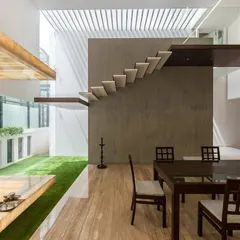 In the Sandeep & Neelam residence, the dining area is designed alongside a sunlit indoor courtyard with synthetic grass. A floating marble pooja room appears to hover over this green space, creating a tranquil spiritual corner.