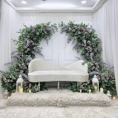 For a touch of classic elegance, we designed this stunning backdrop featuring a white chaise lounge set against a dramatic arch of purple flowers and greenery. The lanterns and candles add a soft, romantic glow.