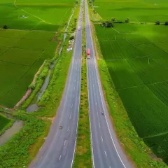 An impressive aerial drone shot of a highway cutting through vibrant green fields, showcasing a symmetrical and powerful perspective.