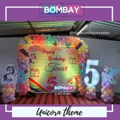 A dreamy unicorn theme for a 5th birthday celebration. This setup includes a custom-printed backdrop, a pastel rainbow balloon frame, unicorn cutouts, and a large light-up number '5'.