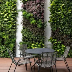 A stylish patio setup with modern outdoor furniture placed in front of several vertical garden panels, creating an intimate and green dining space.