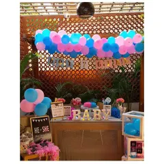 A full view of a gender reveal party setup. The decor includes a 'Boy or Girl' banner, a 'He or She' welcome sign, and light up 'BABY' marquee letters to create a fun and festive corner.
