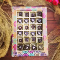 A box of our Handcrafted Artisan Chocolates, ready for gifting. We create various shapes like hearts and squares, each with a unique filling, presented in a beautiful, traditional print box.