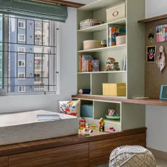 In the 'Poorna' kid's room, a central play area is surrounded by functional elements. A platform bed is set against the window, flanked by a toy storage unit and a spacious study desk with a pin-up board.