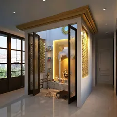 This pooja room is designed as a separate enclosure with foldable glass doors. The golden accents and intricate jaali work on the back wall create a rich and sacred feel.