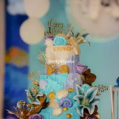 An absolutely stunning cake for an 'Under the Sea' theme, adorned with incredibly detailed, handcrafted sugar seashells, coral, and flowers. It's a masterpiece.