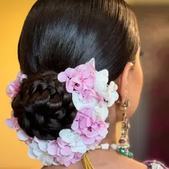 A close-up of a classic bridal bun for a Sikh bride's Anand Karaj ceremony. The sleek, braided bun is elegantly decorated with a garland of pink and white hydrangea flowers, demonstrating a sophisticated and culturally respectful approach to wedding hairstyling.