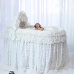 A beautiful, angelic portrait of a baby yawning in an elegant, all-white lace bassinet. This setup creates a dreamy and ethereal look.