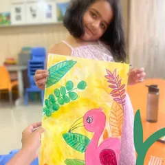 A proud young artist with her vibrant flamingo painting. This piece combines watercolor and drawing, allowing her to explore both blending colors and creating defined lines.