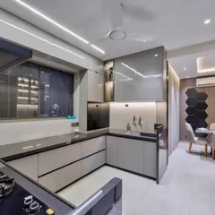 A sleek and modern L-shaped modular kitchen with grey high-gloss cabinets and a black granite countertop. The under-cabinet lighting and glass-fronted upper cabinets add a touch of elegance and improve functionality.