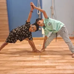 Another pair of boys hold a partner yoga pose, smiling as they help each other balance. We encourage friendship and mutual support in our classes.