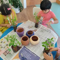 Children carefully transfer saplings into their hand-painted pots. This activity teaches them patience and the basics of plant care.