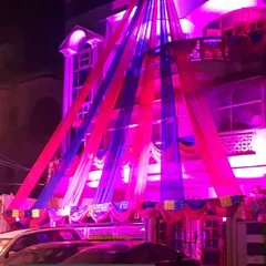 A vibrant nighttime home decoration using blue and pink drapes with bright lighting. This kind of colorful facade decor ensures the wedding house stands out and feels festive.