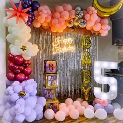 A "Baby" shower or first birthday setup with a silver fringe backdrop. The decoration features 'BABY' blocks, a marquee number '1', and a multi-colored balloon garland.