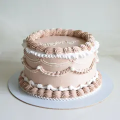 A classic vintage cake with detailed piping work. The design includes delicate swags, ruffles, and shell borders, all in a soft, neutral tone for a timeless and elegant look.