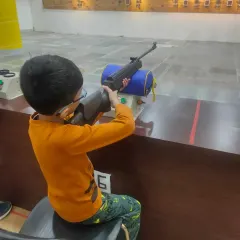 A young student during a basic course session. He is using a support stand to ensure proper form and safety while handling the air rifle.