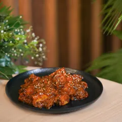 A spicy chicken appetizer, tossed in a thick red sauce and sprinkled with sesame seeds. This behind-the-scenes shot shows the dish just after it's been cooked.