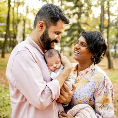 The pure joy and laughter of new parents. This candid shot during an outdoor newborn session captures the happiness a new baby brings. The sleeping baby is cocooned in his dad's arms, completely safe and loved.