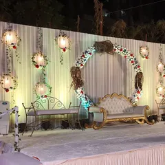 This elegant stage decor features a central floral ring, a classic white and gold sofa, and hanging floral lanterns against a draped white backdrop. The design is perfect for a sophisticated engagement or reception.