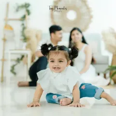 A sweet smile from the star of the show. This shot captures the toddler's playful personality as she crawls, with her parents looking on lovingly in the background.