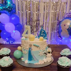 A magical Frozen themed cake and matching cupcakes for a winter wonderland party. The cake features Elsa and Olaf, with edible snowflakes and ice-blue details, creating a scene straight out of Arendelle.