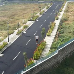 An aerial view of our completed BTM Meadows layout, showing the clean geometry of the asphalt road, paved sidewalks, and regularly spaced streetlights. The planted medians with young trees and shrubs are designed to mature into a green canopy over time.