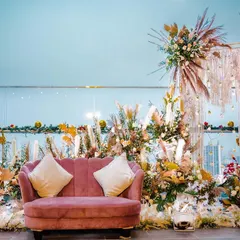 A bohemian-chic photo booth setup against a city skyline. The design uses a dusty rose sofa, pampas grass, and dried floral elements to create a stylish and relaxed atmosphere perfect for a modern brand activation.
