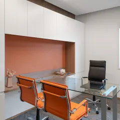 A private cabin in 'The High-Flying Office' features a glass desk and vibrant orange chairs, continuing the brand's color scheme. The space is designed for comfort and functionality, with ample storage and a view of the surrounding greenery.