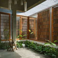 The courtyard at "The Mantle" features modern jaali-inspired screens. These wooden screens provide privacy and ventilation while casting intricate light patterns, a contemporary take on a traditional Indian feature.