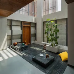 This internal courtyard features a floor of dark, locally sourced stone, which grounds the space. The surrounding walls are made of textured concrete blocks, creating a rich material palette that is animated by the play of natural light.