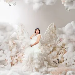 An ethereal portrait of a mother-to-be with butterfly-like wings, standing amidst a sea of clouds and flowers. This heavily edited, dreamy image creates a magical, fairy-tale scene.
