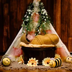 A sweet 'bumblebee' themed newborn shoot, with the baby sleeping soundly in a basket inside a floral teepee, surrounded by crocheted bees.