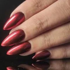 A close-up of the intense red chrome finish on a sharp stiletto nail, showcasing the flawless, mirror-like surface.