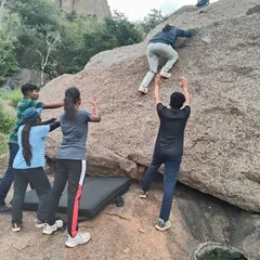A climber is carefully spotted by her teammates and an instructor during a bouldering session. We use crash pads and proper spotting techniques to ensure a safe learning environment.