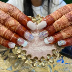 A full view of a gorgeous bridal nail set against the client's henna. The combination of white, glitter, and crystals is a timeless choice.
