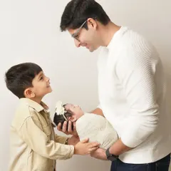 A young boy looks up at his father, who is holding his new baby sister. This image beautifully captures the moment a child is introduced to their new sibling.