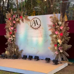 A beautiful boho-chic stage for an outdoor sangeet, with pampas grass arches, a marble-effect backdrop, and a custom monogram.