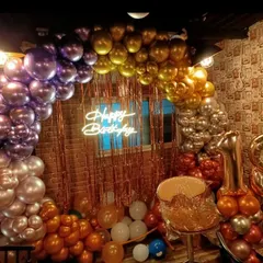An 18th birthday setup in a cafe, designed to feel trendy and celebratory. I used a mix of metallic chrome balloons in purple, gold, and rose gold to create a rich arch, complemented by a shimmery curtain and a neon sign.
