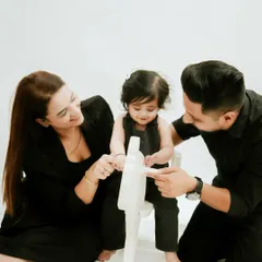 A candid moment of play. The parents interact with their daughter on a rocking horse, creating a natural and loving family photograph.