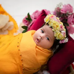 An awake newborn with bright eyes is swaddled in a beautiful yellow drape, wearing a floral crown. We are experienced in capturing both sleeping and awake babies, showcasing their curious and alert expressions.