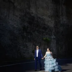 A full-length view of a couple walking together, showcasing their stylish outfits against a dark, textured cliffside. This is part of a series from a destination shoot in Bali.