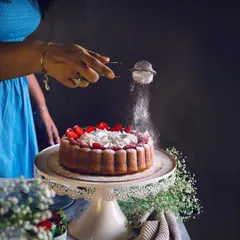 The baker's hands dusting a beautiful strawberry cake, showcasing the personal touch that goes into every creation.